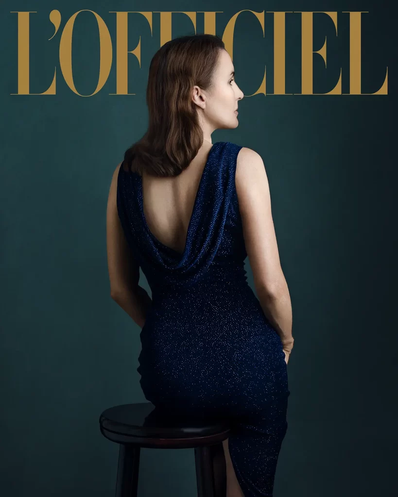 L'Officiel magazine cover. Woman sitting on a stool in a sparkling blue evening dress on a green background.
