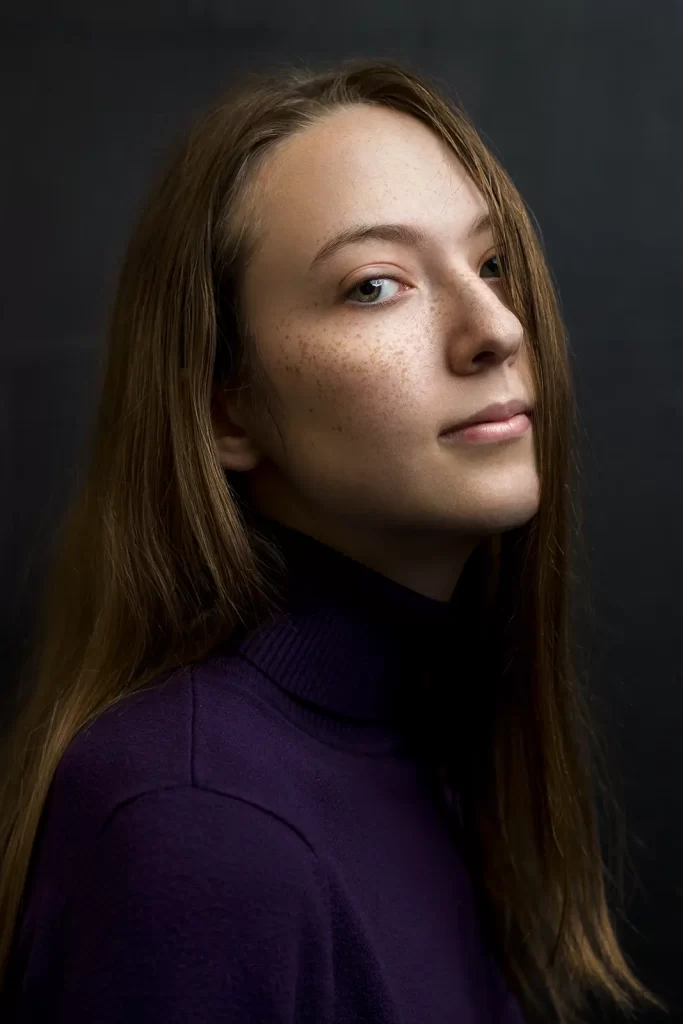 Mysterious teenage girl in a purple sweater on a dark background.