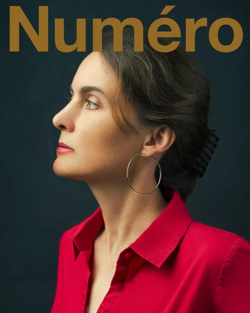 Numero magazine cover. Woman in a red blouse wearing a gold hoop earring on a green background.
