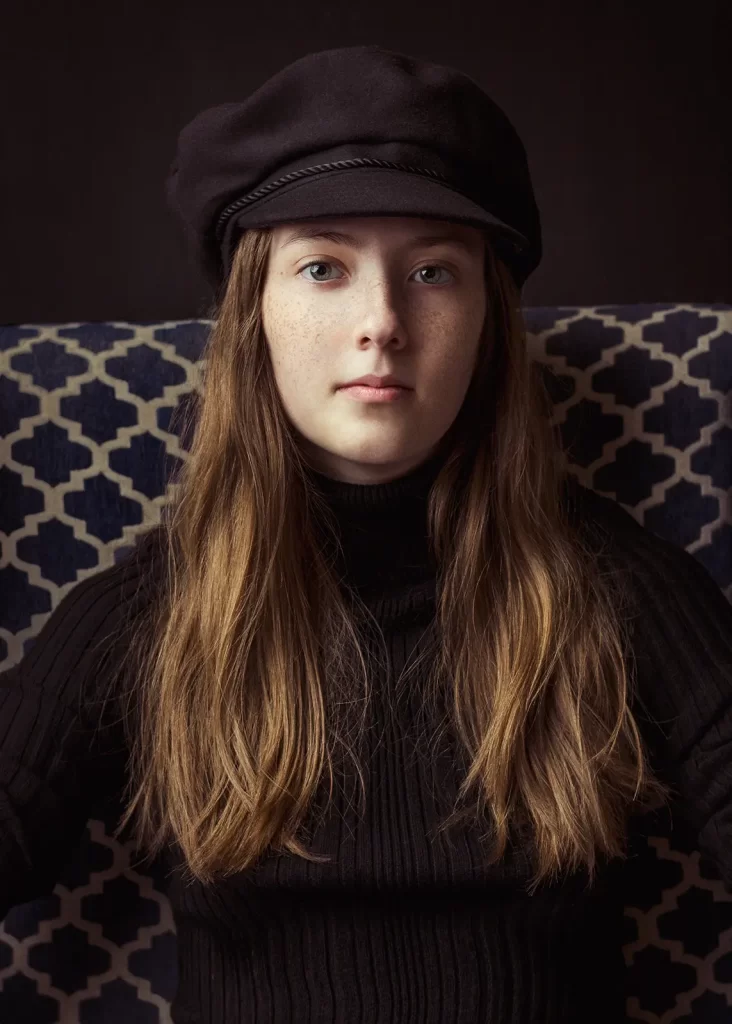 Teenage girl with long hair wearing a black turtleneck and a biker hat.