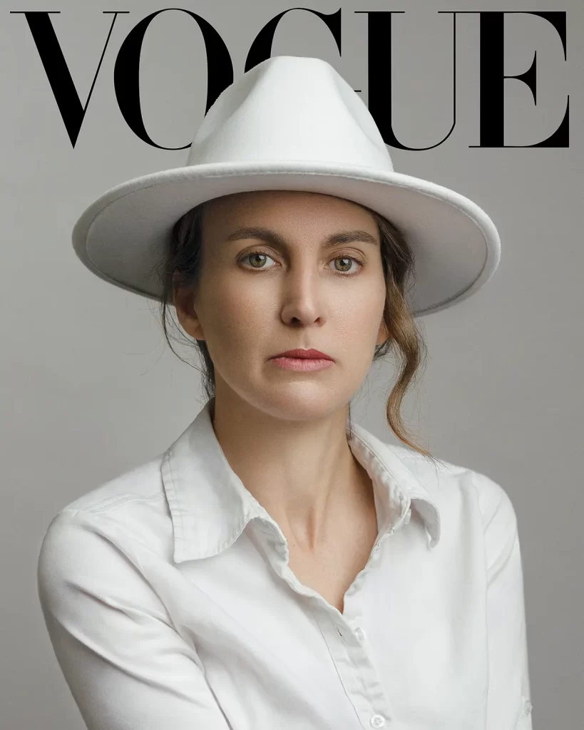 Vogue magazine cover. Woman in a white blouse wearing a white hat on a gray background.