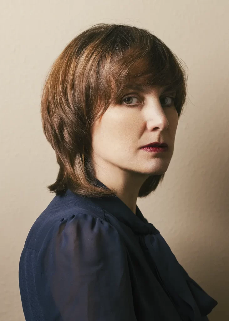 Attractive woman in a navy blue blouse with short brown hair on a light background.