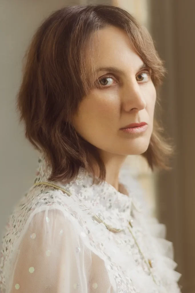 Attractive woman in a frilly white blouse with short brown hair bathed in warm window light.