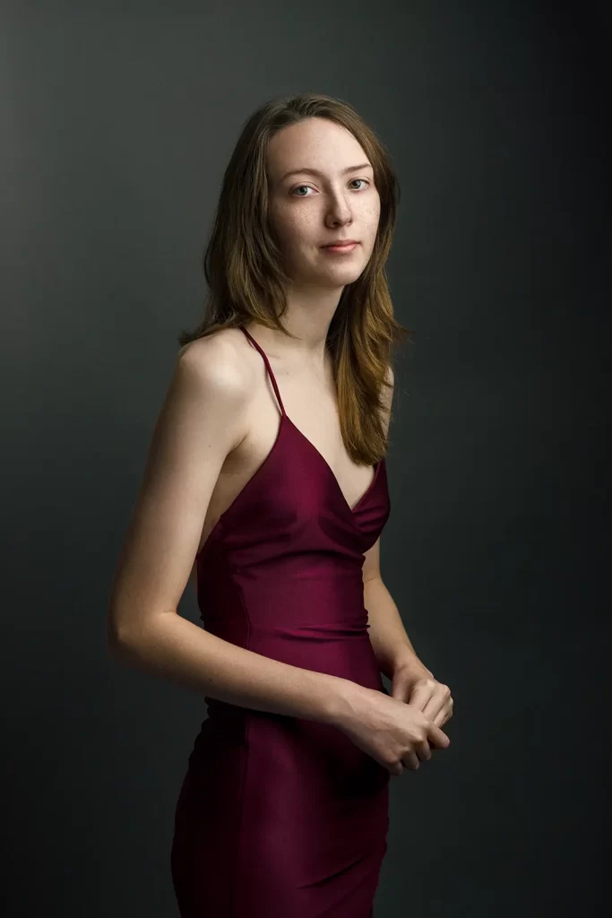 Teenage girl in a maroon evening dress on a dark background.