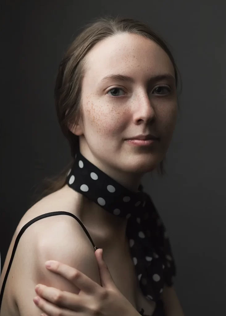 Chromatic portrait of a teenage girl with hair pulled back wearing a polka dot scarf on a dark background.