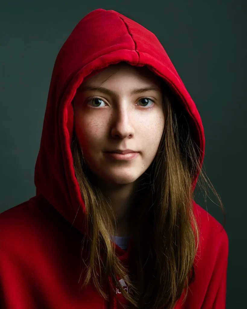 Teenage girl in a red hoodie on a dark green background.