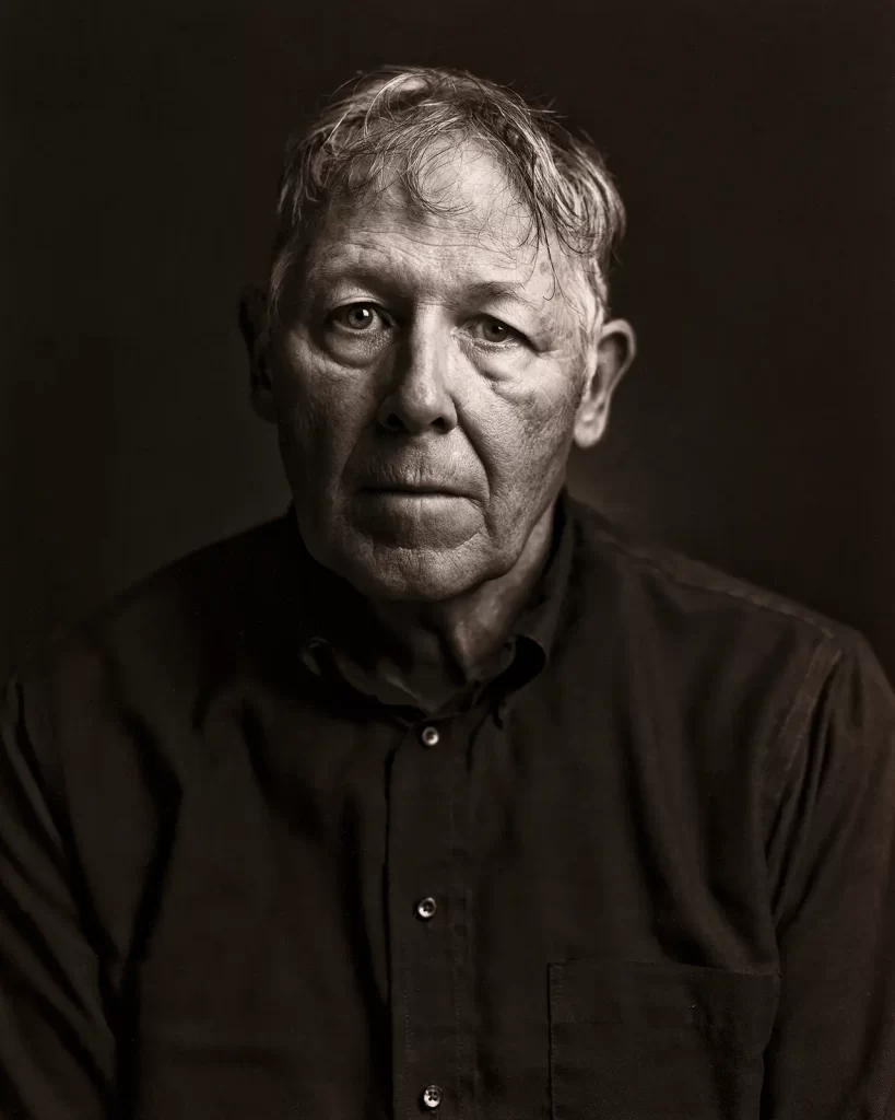 Black and white contact print of an old man in a black shirt on a black background.