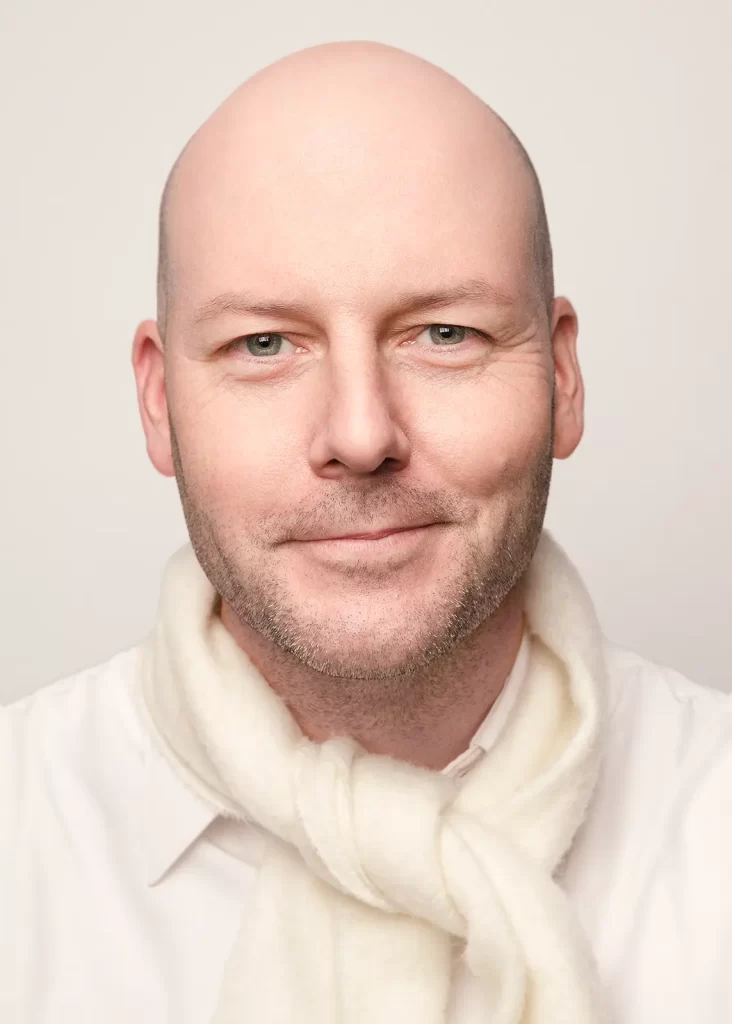 Middle-aged bald man wearing a white scarf on a white background.