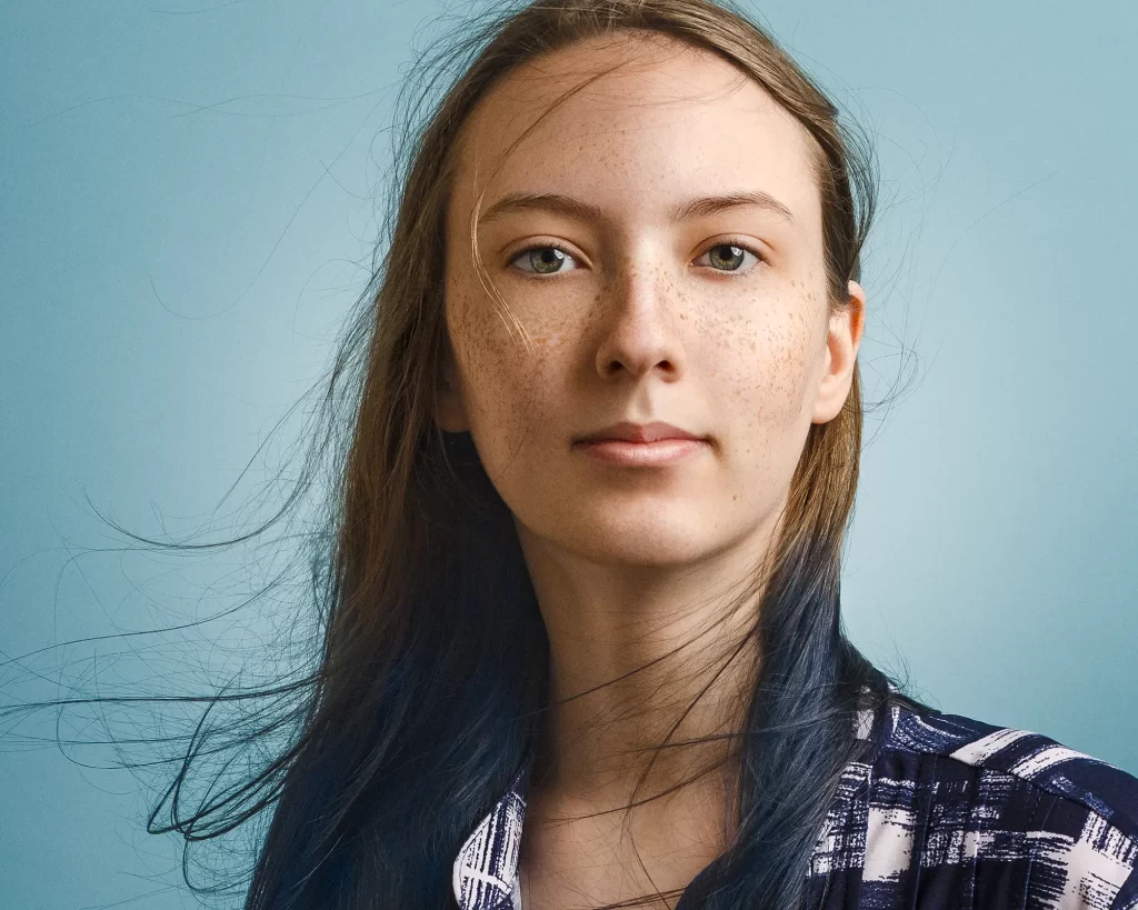 Teenage girl with dark blue hair blowing in the wind on a light blue background.