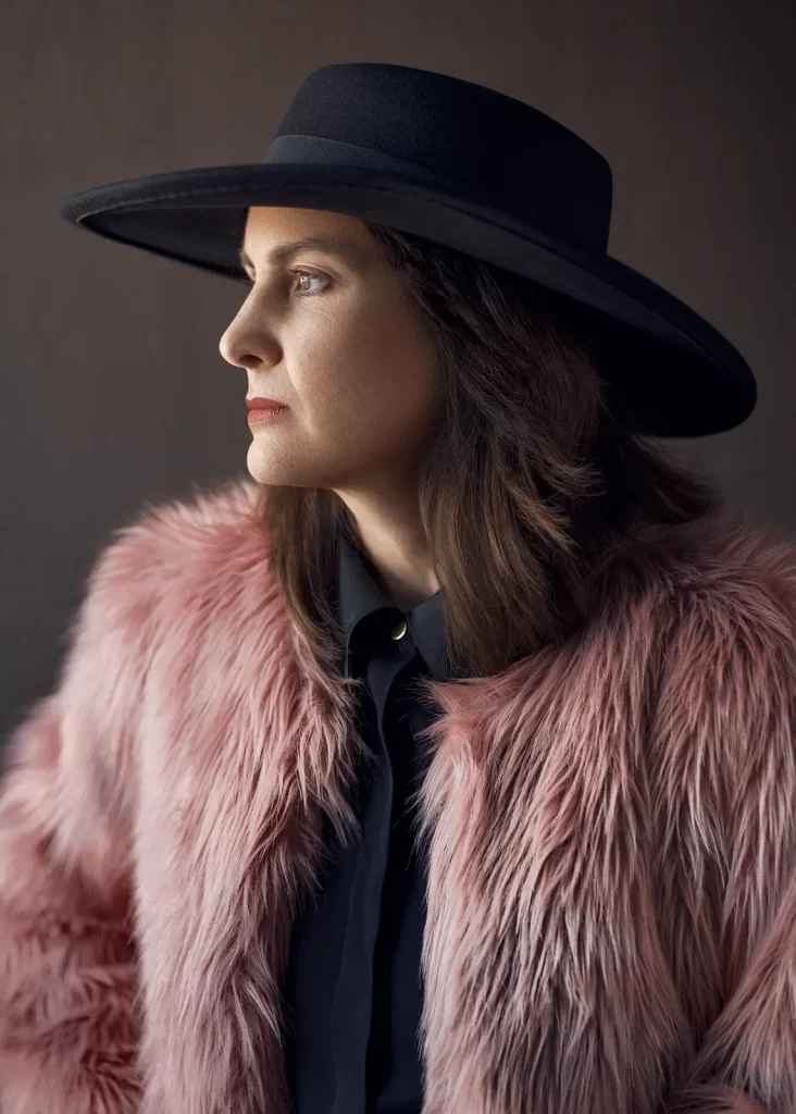 Attractive brunette woman with long hair wearing a black hat and a fuzzy pink jacket.
